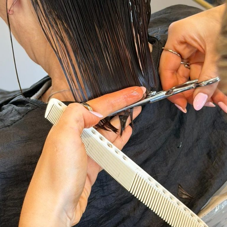 Hair Cutting A person's hand holding a comb beside scissors cutting long hair.